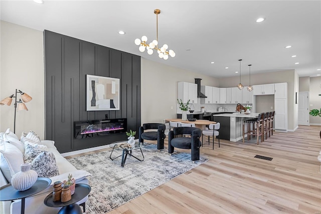 living area featuring a notable chandelier, recessed lighting, visible vents, a large fireplace, and light wood-type flooring