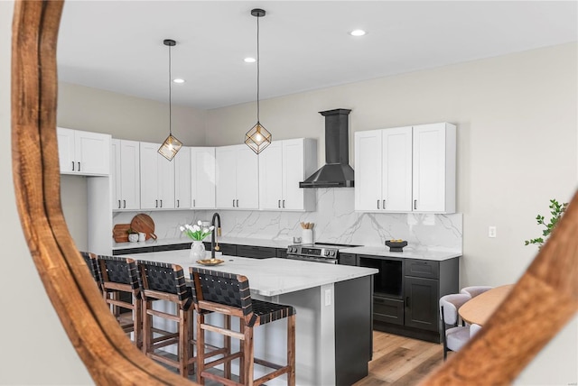 kitchen featuring a breakfast bar, stainless steel range with electric cooktop, wall chimney range hood, white cabinetry, and backsplash