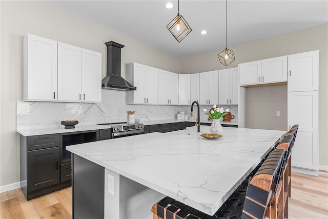 kitchen with decorative backsplash, stainless steel electric range oven, light stone countertops, light wood-type flooring, and wall chimney range hood