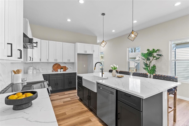 kitchen featuring light stone counters, a sink, white cabinets, stainless steel dishwasher, and backsplash