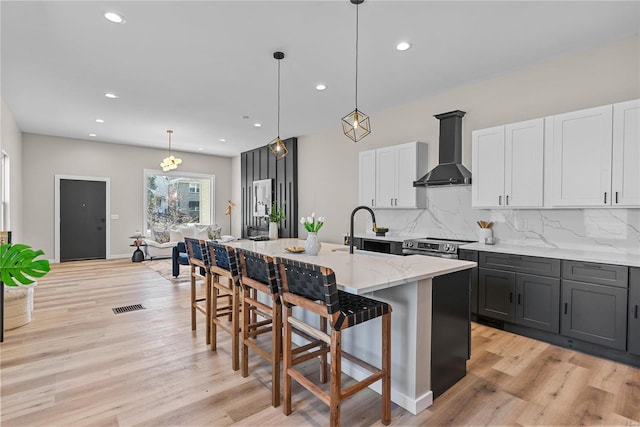 kitchen featuring a breakfast bar area, a sink, light wood-type flooring, wall chimney exhaust hood, and tasteful backsplash