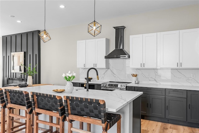 kitchen featuring wall chimney range hood, stainless steel electric range, backsplash, and light stone counters