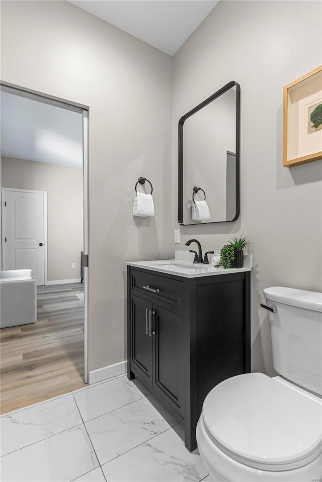 half bath with marble finish floor, vanity, toilet, and baseboards