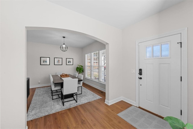 foyer featuring arched walkways, baseboards, and wood finished floors