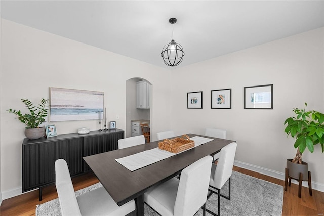 dining space featuring arched walkways, a notable chandelier, baseboards, and wood finished floors