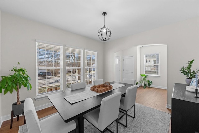 dining space with an inviting chandelier, baseboards, arched walkways, and wood finished floors