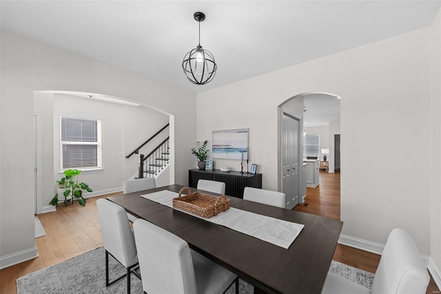 dining area with baseboards, stairs, arched walkways, and wood finished floors