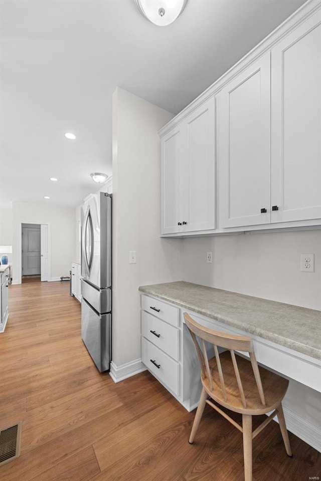 kitchen with built in desk, visible vents, light wood-style flooring, freestanding refrigerator, and white cabinets