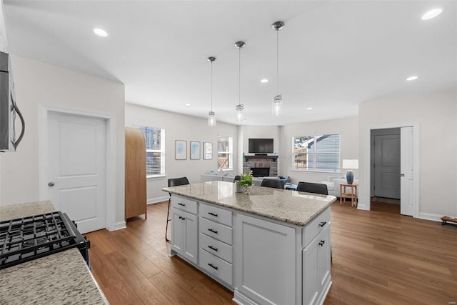 kitchen with dark wood finished floors, a kitchen island, open floor plan, a fireplace, and pendant lighting