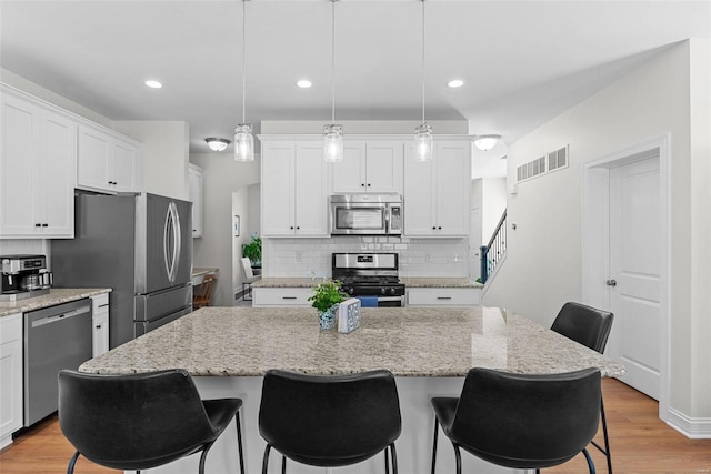 kitchen with white cabinets, light wood-type flooring, appliances with stainless steel finishes, and a kitchen breakfast bar