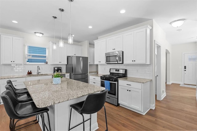 kitchen with arched walkways, a breakfast bar area, stainless steel appliances, a sink, and wood finished floors