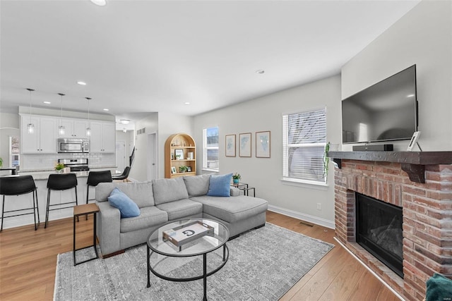 living room featuring recessed lighting, a fireplace, visible vents, baseboards, and light wood finished floors