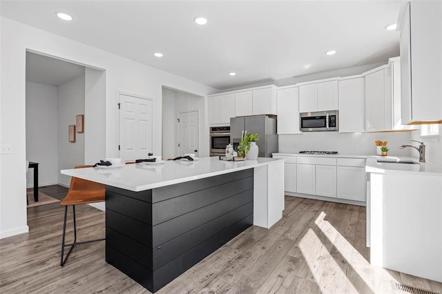 kitchen featuring stainless steel appliances, a center island, white cabinets, and a sink