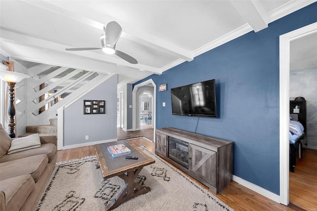 living area featuring arched walkways, beamed ceiling, wood finished floors, and baseboards