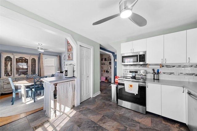 kitchen featuring tasteful backsplash, appliances with stainless steel finishes, a ceiling fan, stone finish floor, and white cabinets