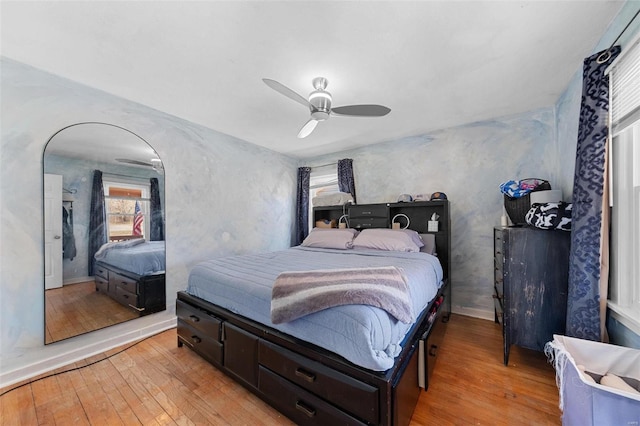 bedroom with light wood-style floors, arched walkways, and a ceiling fan