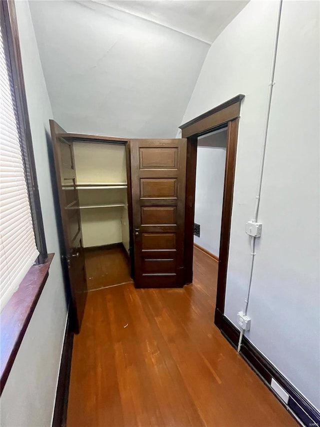 hallway featuring vaulted ceiling, dark wood-type flooring, and baseboards