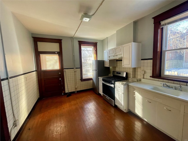 kitchen featuring under cabinet range hood, a wainscoted wall, stainless steel appliances, a sink, and dark wood finished floors