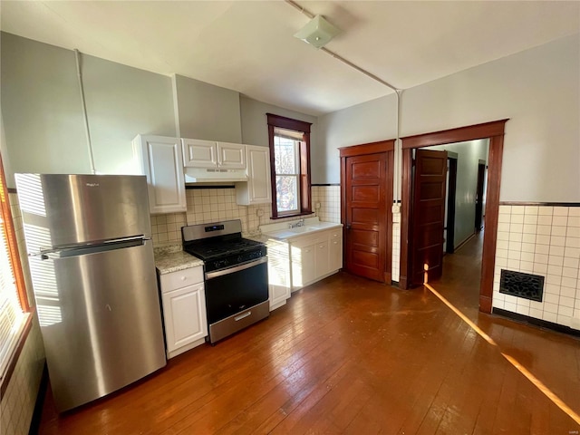 kitchen featuring white cabinets, dark wood-style floors, stainless steel appliances, under cabinet range hood, and a sink