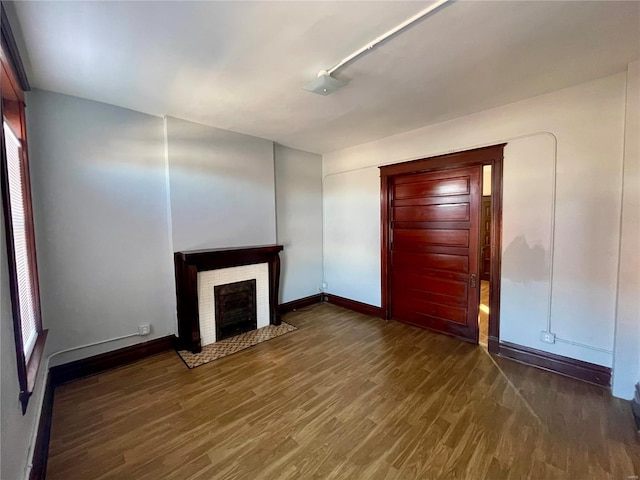 unfurnished living room with a brick fireplace, wood finished floors, and baseboards