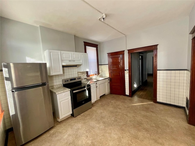 kitchen featuring under cabinet range hood, a wainscoted wall, a sink, white cabinets, and appliances with stainless steel finishes