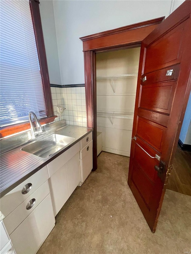 kitchen featuring stainless steel countertops, white cabinetry, and a sink