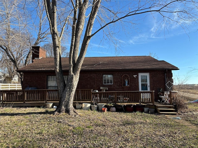 rear view of house with brick siding, a chimney, a lawn, and a wooden deck