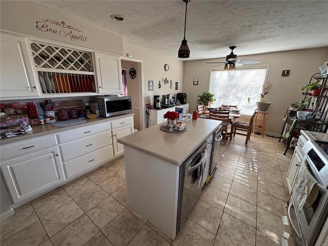 kitchen featuring light countertops, stainless steel microwave, stove, white cabinetry, and a kitchen island