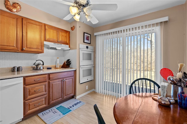 kitchen with light wood-style flooring, backsplash, brown cabinetry, white appliances, and under cabinet range hood