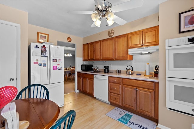 kitchen featuring white appliances, light wood-style flooring, light countertops, under cabinet range hood, and backsplash