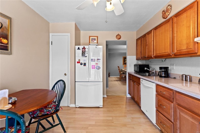 kitchen featuring brown cabinets, light countertops, light wood-style flooring, decorative backsplash, and white appliances