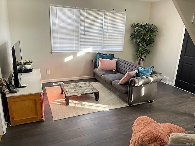 living room with dark wood-style floors, visible vents, and baseboards