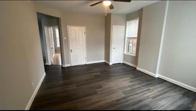 unfurnished bedroom with multiple windows, dark wood finished floors, and baseboards