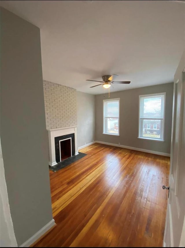 unfurnished living room with ceiling fan, a fireplace, baseboards, and wood finished floors