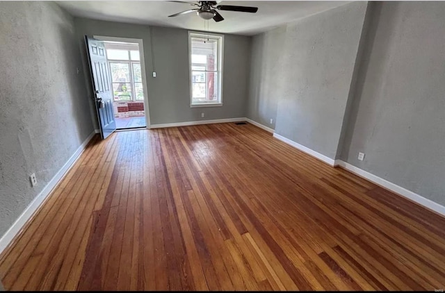 interior space with a textured wall, hardwood / wood-style floors, a ceiling fan, and baseboards