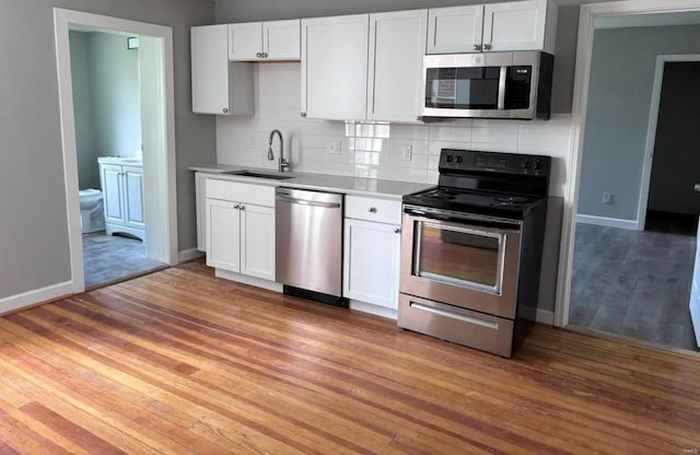 kitchen with stainless steel appliances, a sink, light wood-style floors, white cabinets, and backsplash