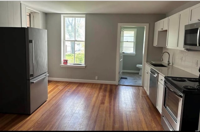 kitchen with appliances with stainless steel finishes, plenty of natural light, a sink, and hardwood / wood-style flooring