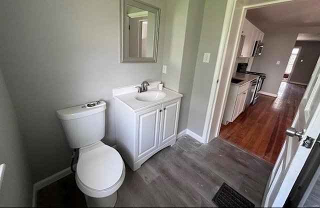 half bath with vanity, wood finished floors, toilet, and baseboards