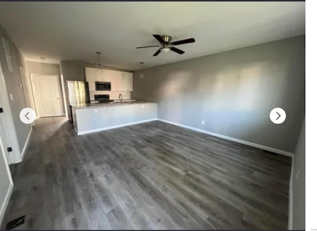 unfurnished living room with a sink, dark wood-style floors, baseboards, and a ceiling fan