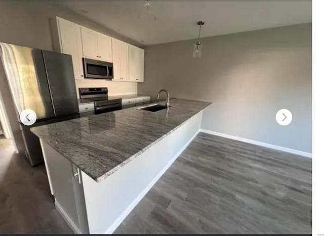 kitchen with stainless steel appliances, a peninsula, a sink, white cabinetry, and dark wood-style floors