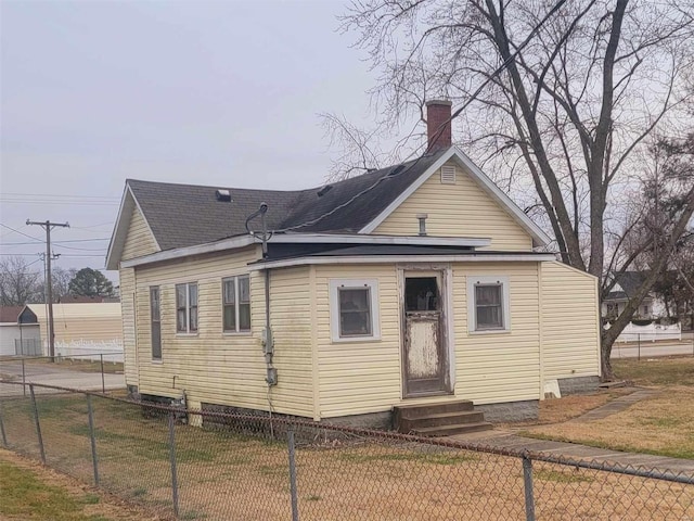 rear view of property with entry steps, fence, a chimney, and a lawn