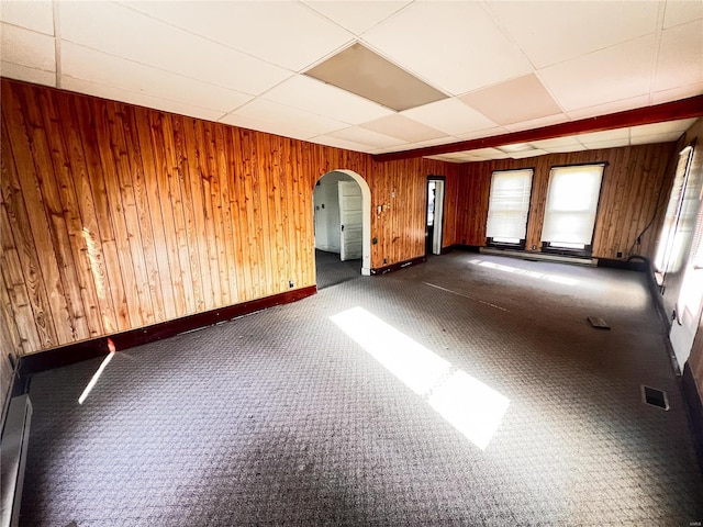 unfurnished room featuring visible vents, wooden walls, baseboards, arched walkways, and a paneled ceiling