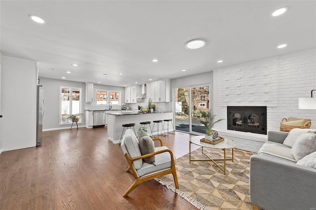 living room with dark wood-style floors, a brick fireplace, baseboards, and recessed lighting