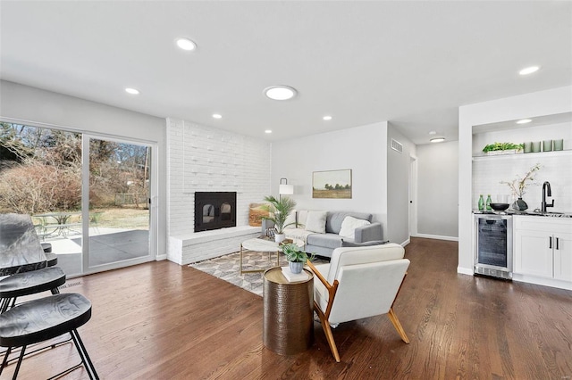 living area with wine cooler, dark wood-style flooring, indoor wet bar, recessed lighting, and a brick fireplace