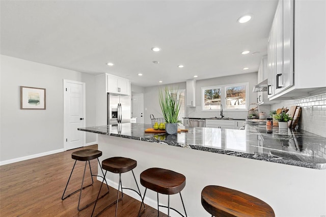 kitchen featuring dark stone counters, appliances with stainless steel finishes, dark wood-style flooring, a peninsula, and a sink