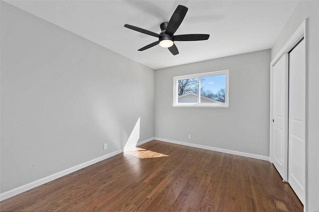 unfurnished bedroom with dark wood-type flooring, a closet, baseboards, and a ceiling fan