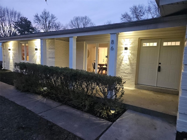 doorway to property featuring brick siding and a porch