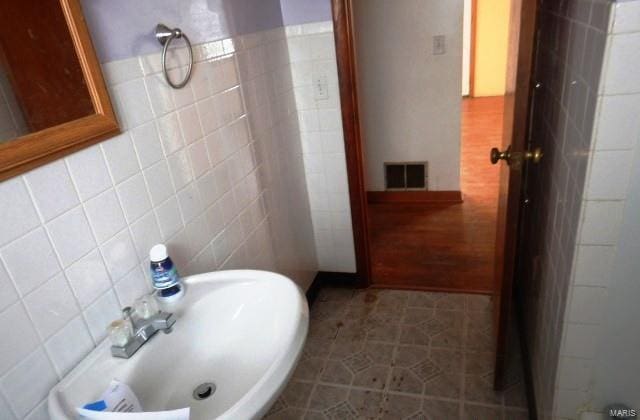 bathroom featuring tile patterned flooring, a sink, visible vents, and tile walls