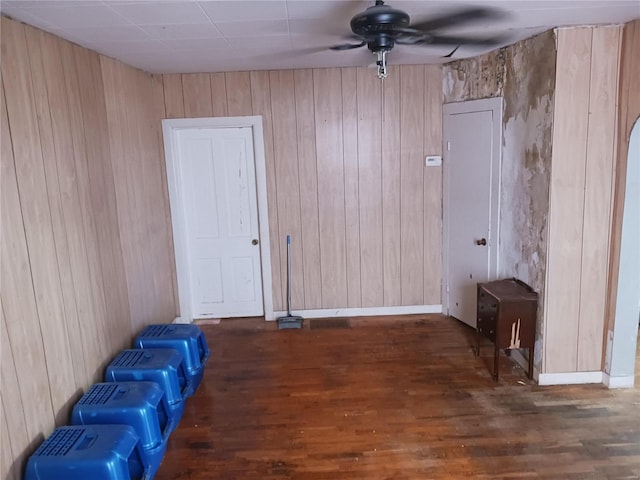 empty room with dark wood-type flooring, wooden walls, baseboards, and a ceiling fan