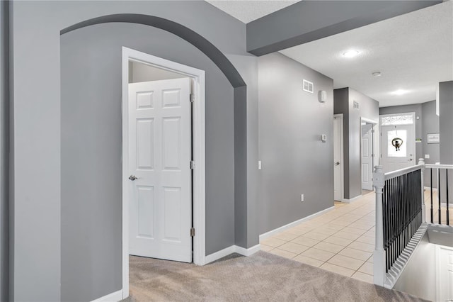 corridor with arched walkways, a textured ceiling, visible vents, and light colored carpet